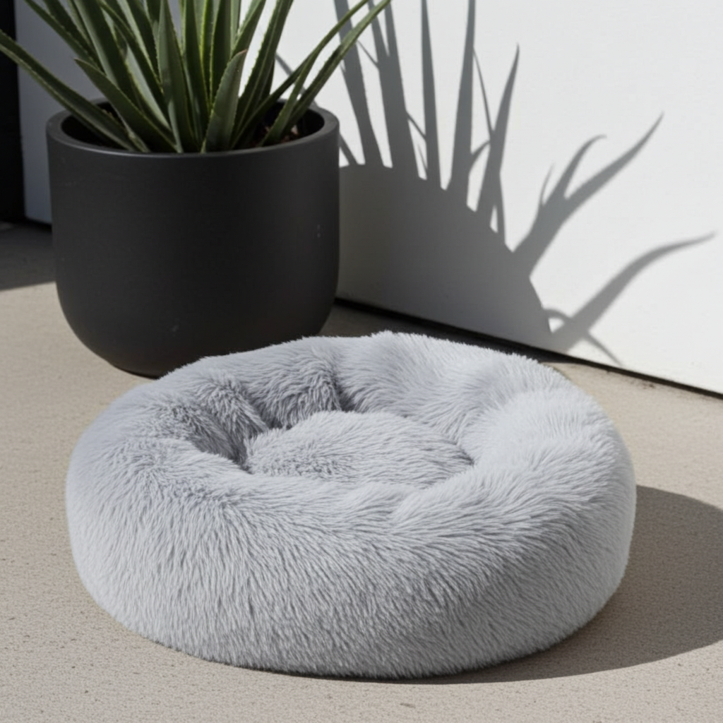Fluffy gray pet bed on a concrete floor with a plant in the background