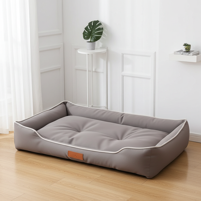 Gray pet bed on a wooden floor with a white wall and plant in the background
