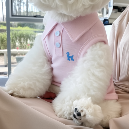 White fluffy dog wearing a pink outfit with blue buttons, sitting on a person's lap.